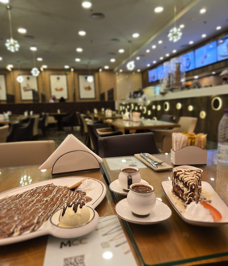 A table at MCC cafe with desserts and coffee, featuring a crepe, cake, and two cups of coffee.