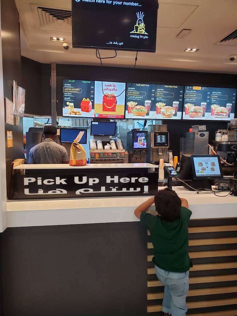 A child waits at the McDonald's counter with digital menus displaying food items.