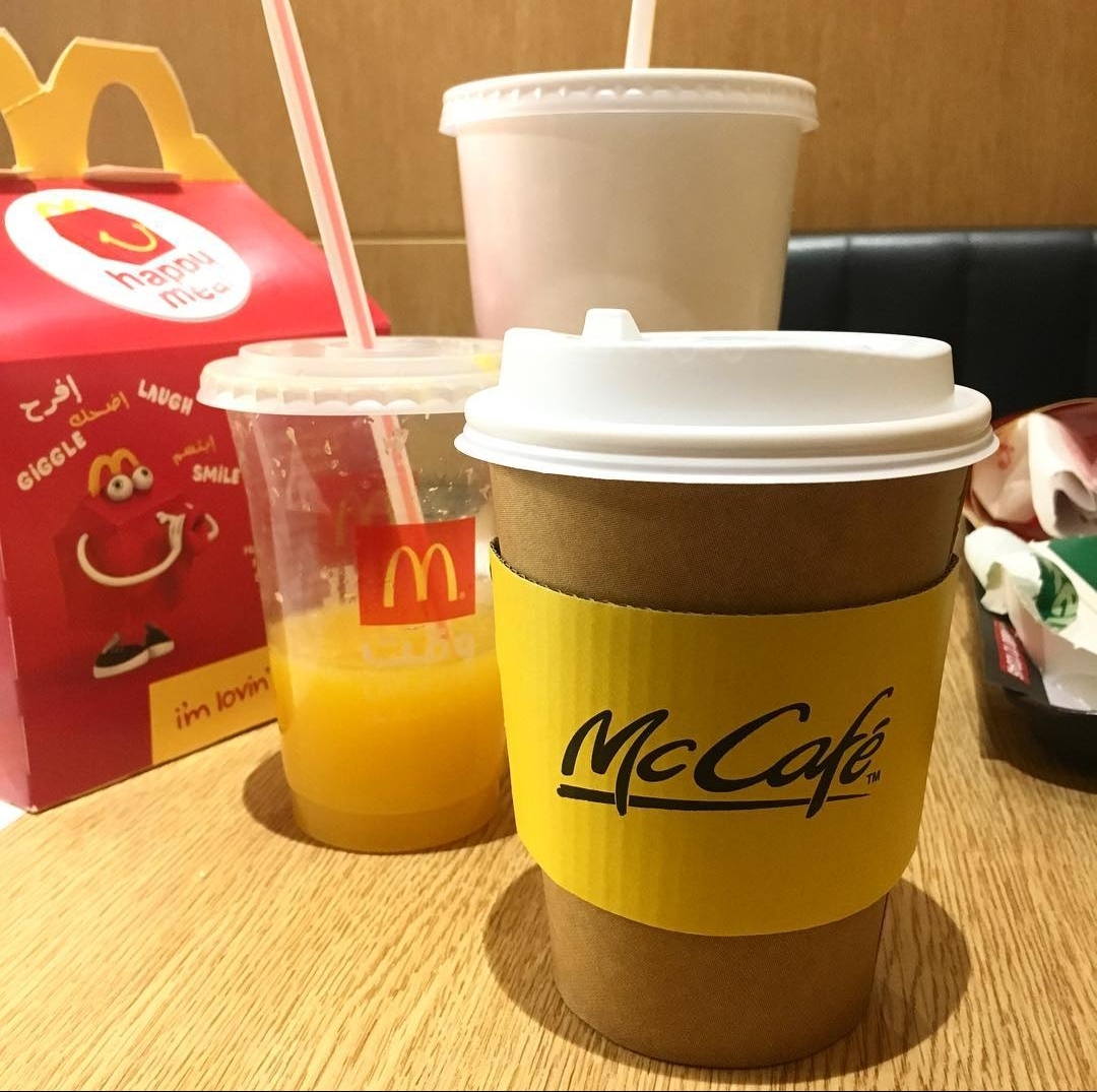 A McDonald's Happy Meal box, orange juice, and McCafe coffee on a wooden table.