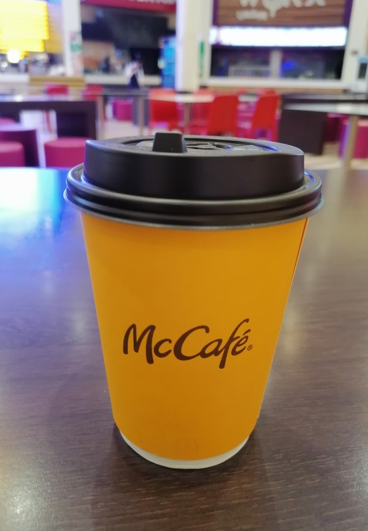 A McCafe branded coffee cup with a black lid sits on a wooden table.
