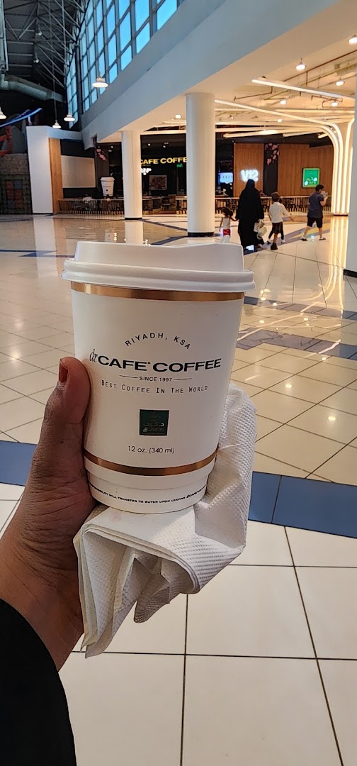 A hand holds a cup of coffee from Dr. Cafe Coffee in a mall.