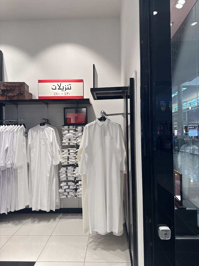 Interior view of a clothing store displaying traditional white thobes and folded shirts.