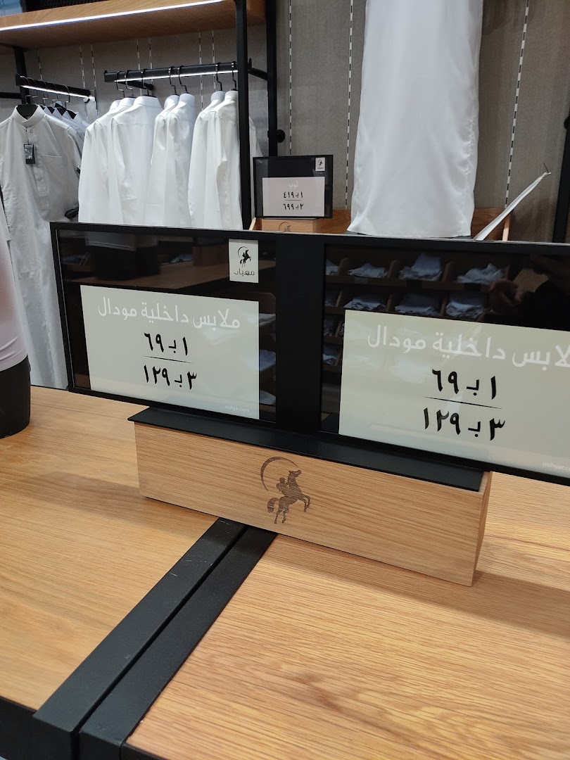 White thobes displayed on racks with price signs in Arabic.