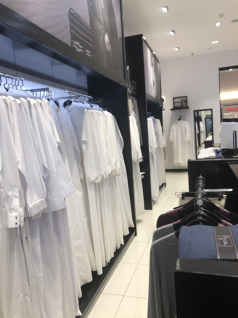Interior view of a clothing store displaying rows of white thobes and other garments on hangers.