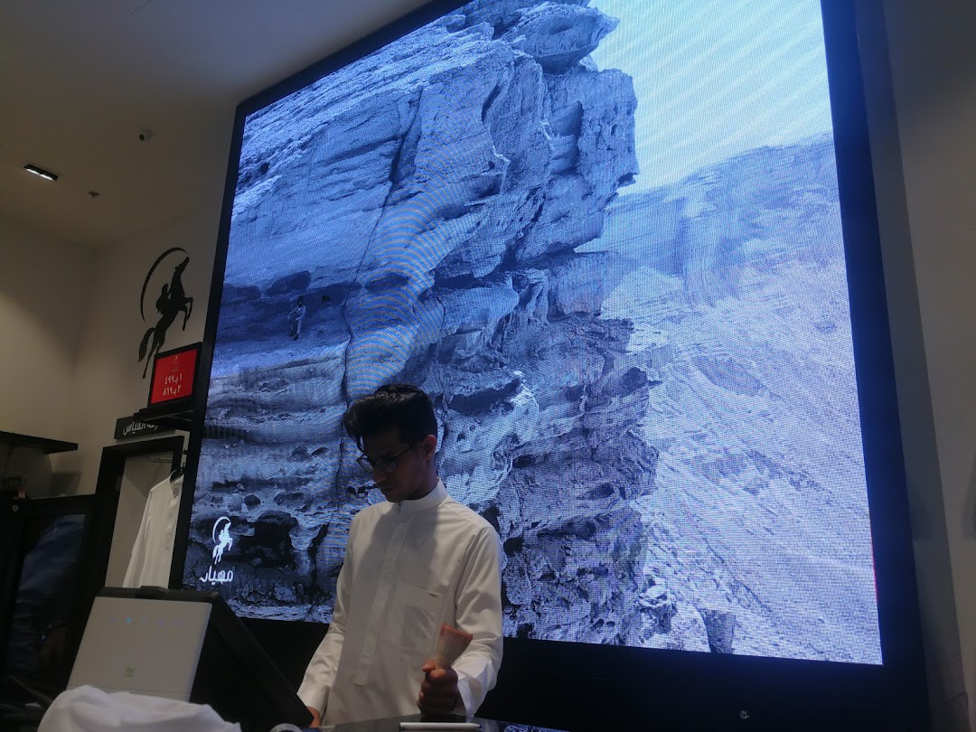 A man in traditional attire stands in front of a large digital screen displaying a rocky landscape.
