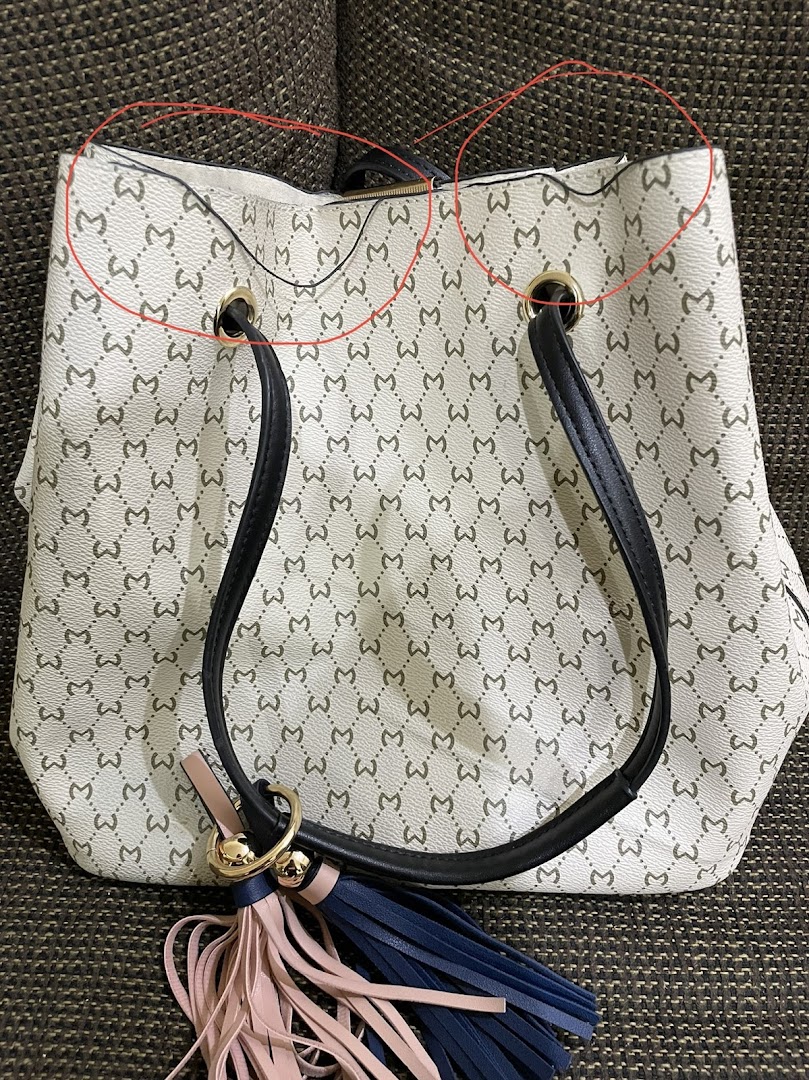 A white tote bag with a repeating pattern of the letter 'M' and tassels.