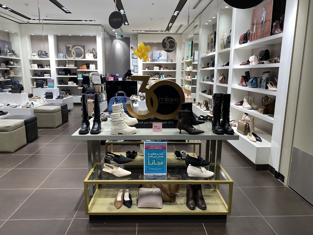 Interior view of a Milano shoe store showcasing various footwear and handbags on shelves and display tables.