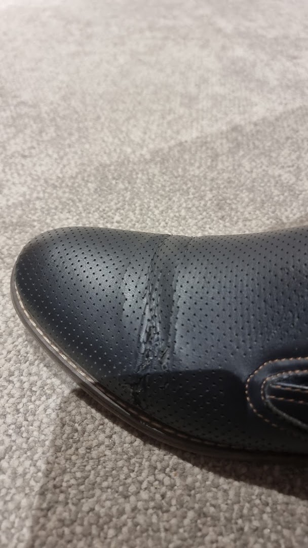 A close-up shot of a damaged black leather shoe with perforated detailing.