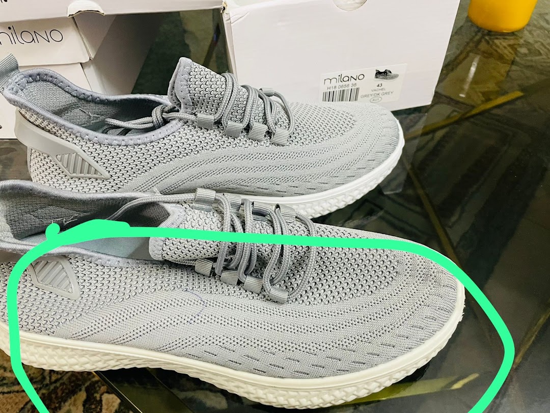 A pair of grey knitted sneakers from Milano are displayed on a table with their boxes.