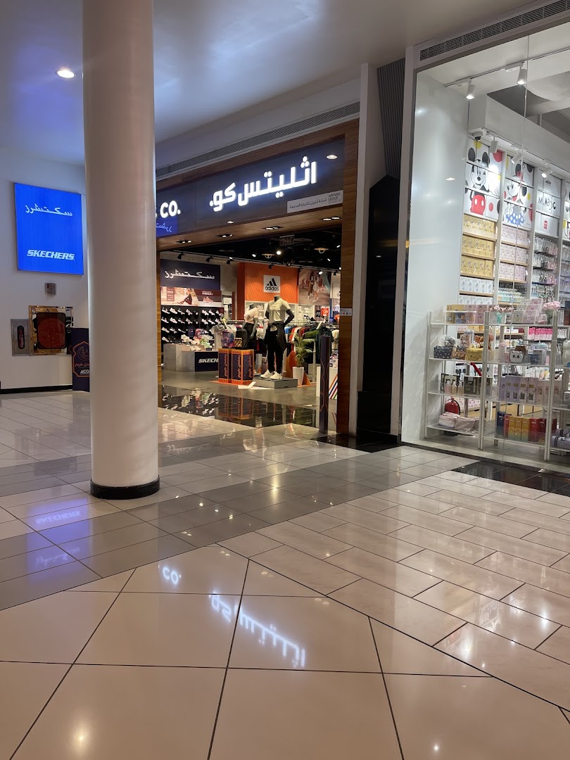 A view of a shopping mall corridor with two distinct shops, one selling athletic wear and the other various merchandise.