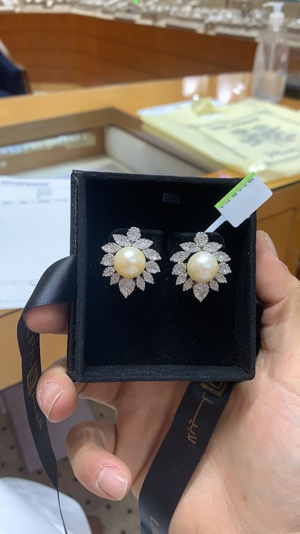 A hand holds a jewelry box containing pearl and diamond earrings.