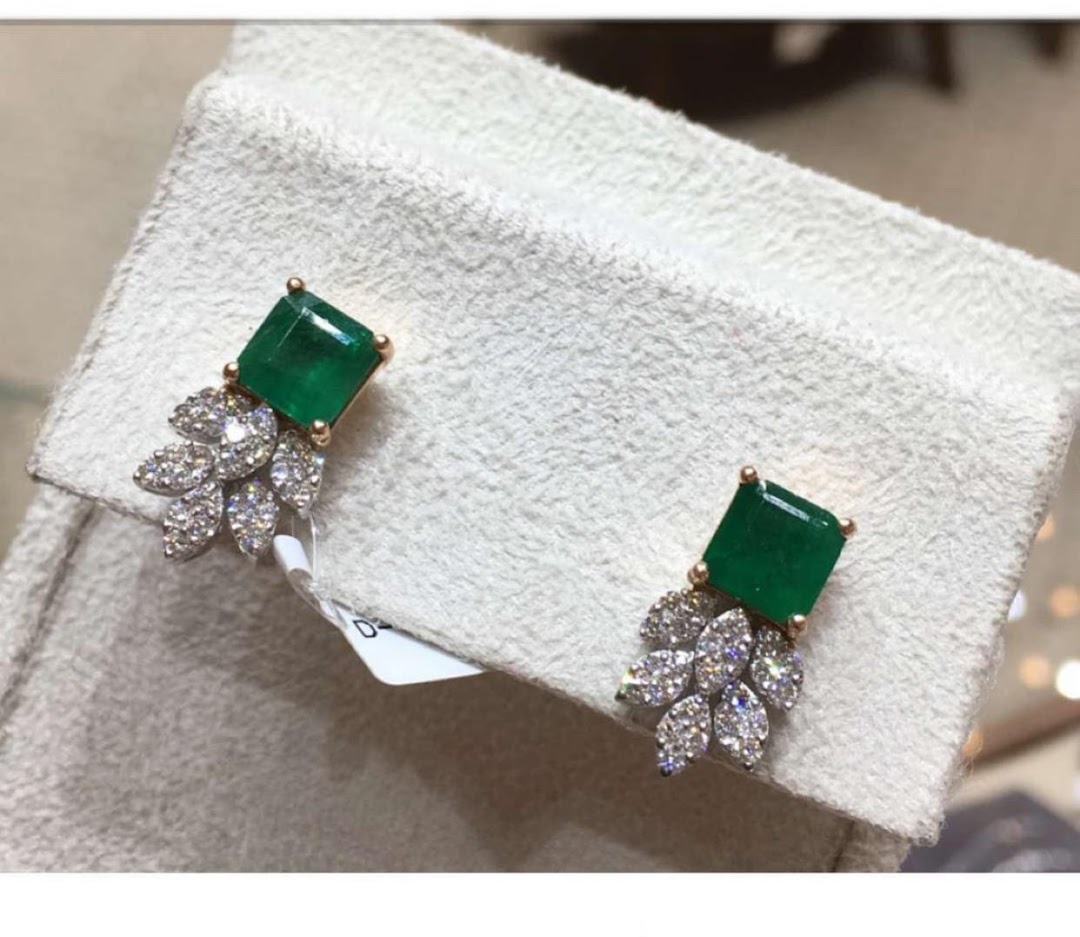 A pair of exquisite emerald and diamond earrings displayed on a textured white surface.
