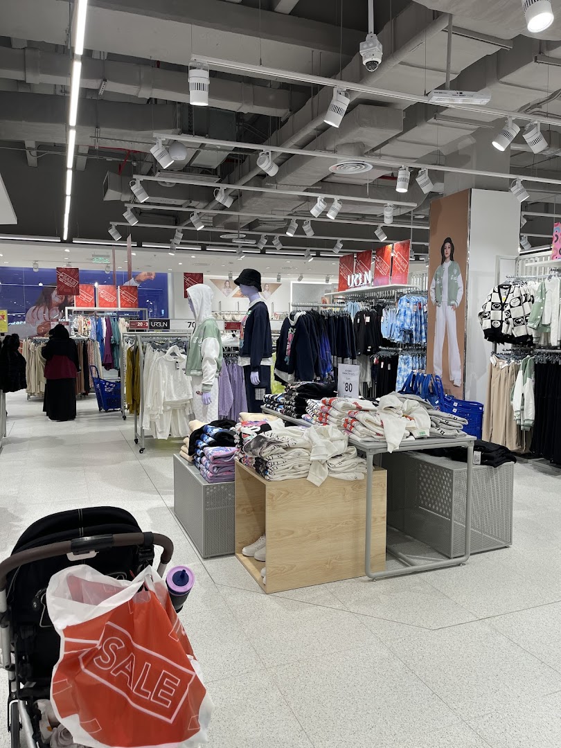 Interior view of a clothing store with racks of apparel, mannequins, and a shopping cart.