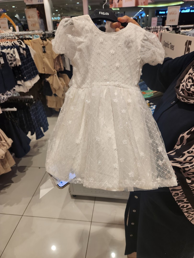 A person holds up a white, sparkly dress with floral details in a clothing store.