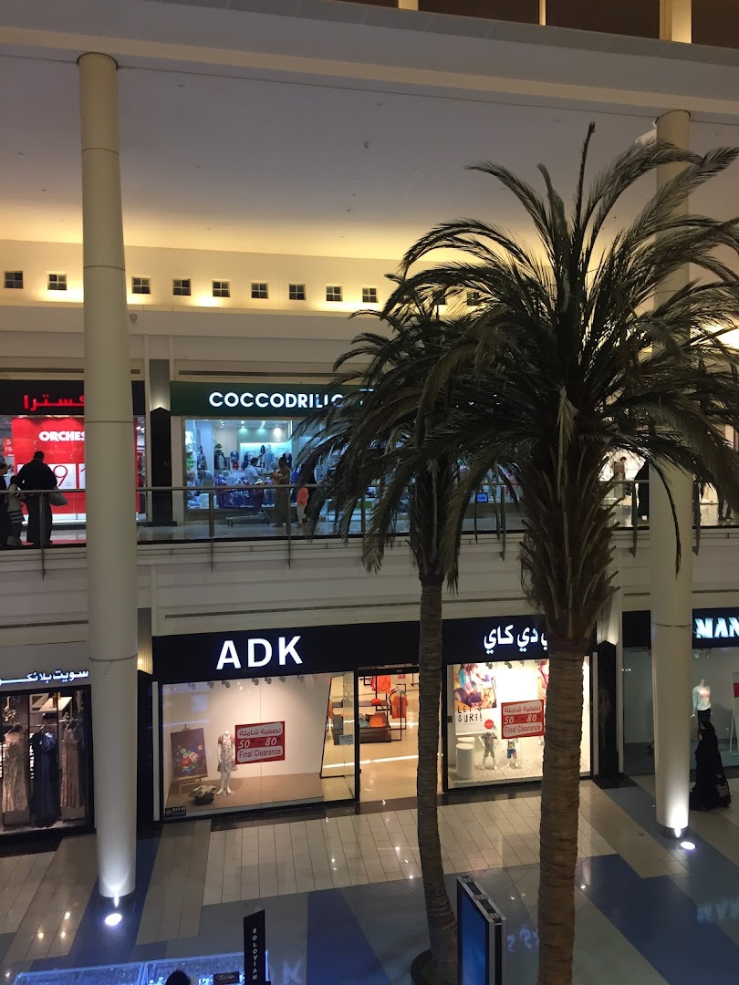 A view of several shops in a mall, including ADK and Coccocrilic, with palm trees in the foreground.