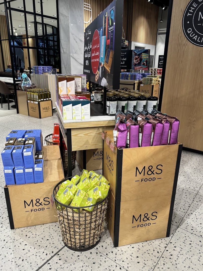 A display of M&S Food products including tea, coffee, and snacks in wooden crates and baskets.