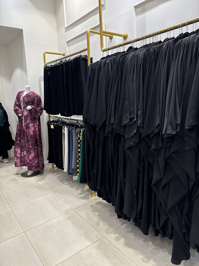 A shop interior displaying a variety of abayas and modest wear on hangers and a mannequin.