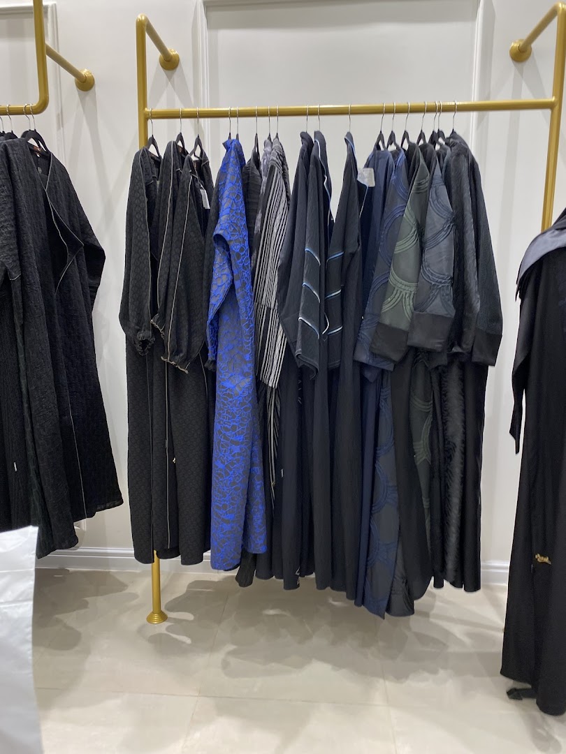 A rack of elegant abayas in various black and blue designs, displayed in a boutique.