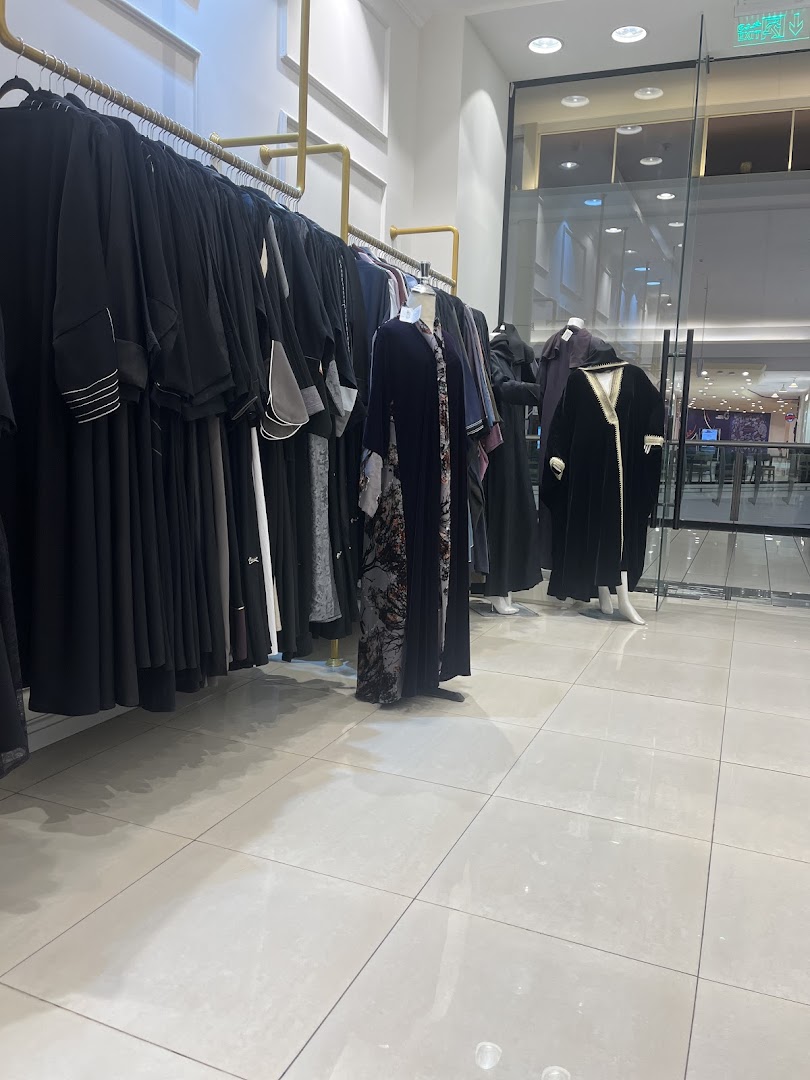 A shop interior displaying a variety of elegant abayas on hangers and mannequins.