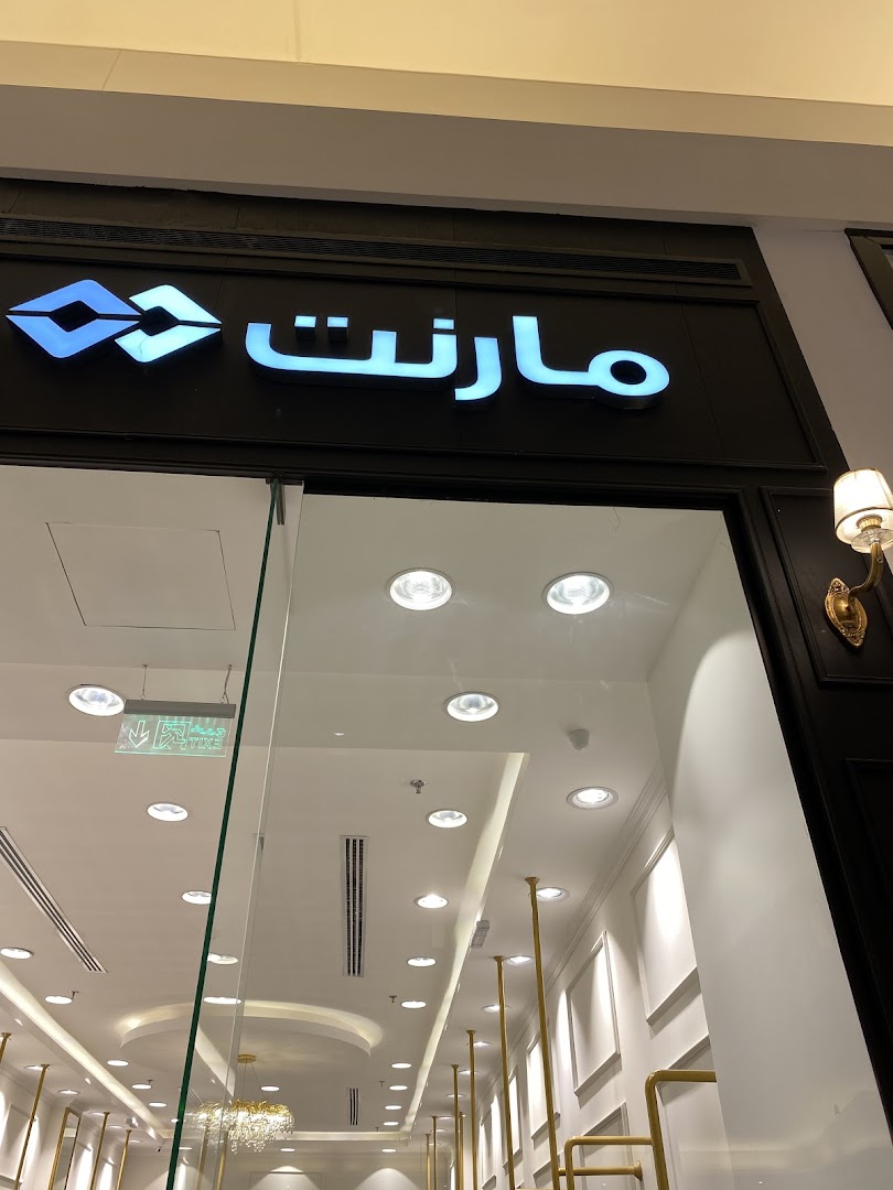 The illuminated sign of 'مشغل مارنت فرع غرناطة مول' above a shop entrance.