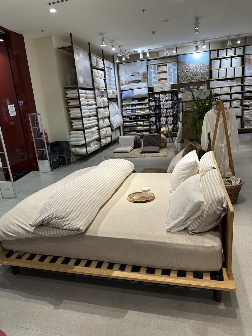 A Muji store interior showcasing a neatly made bed with pillows and bedding, surrounded by shelves of products.