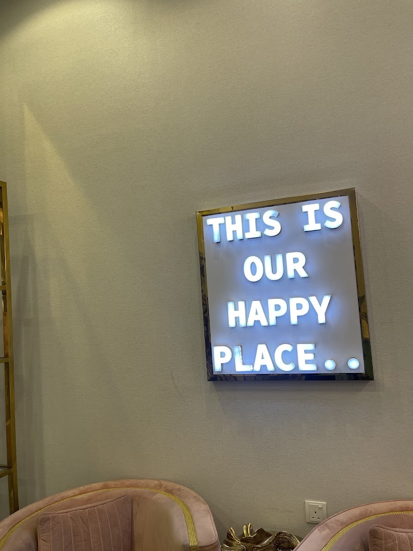 A lit sign saying 'THIS IS OUR HAPPY PLACE' hangs on a wall above plush pink chairs.