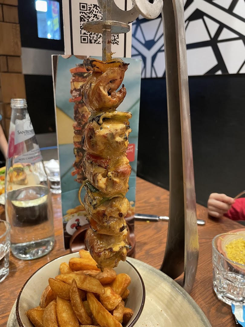 A close-up of a chicken skewer with fries, served at a restaurant.