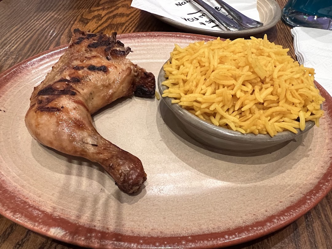 A grilled chicken leg quarter served with a side of fluffy yellow rice on a plate.