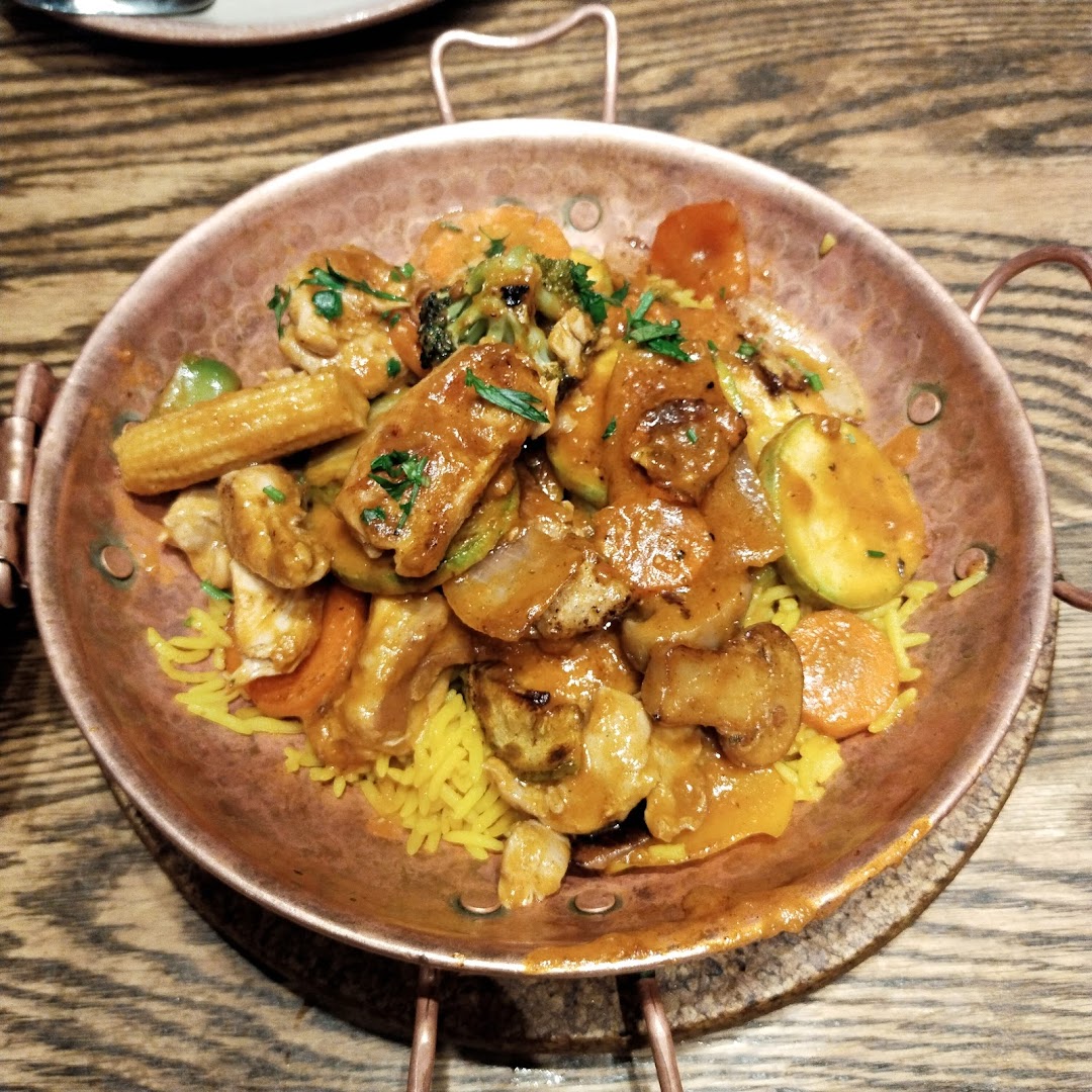 A close-up of a flavorful chicken and vegetable dish served with yellow rice in a copper bowl.