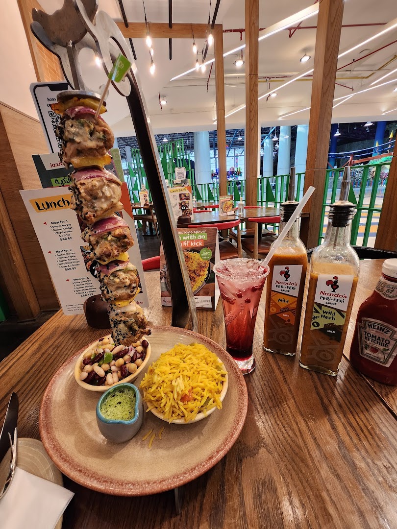A Nando's meal featuring a skewer of chicken, rice, beans, and sauces, with a drink.