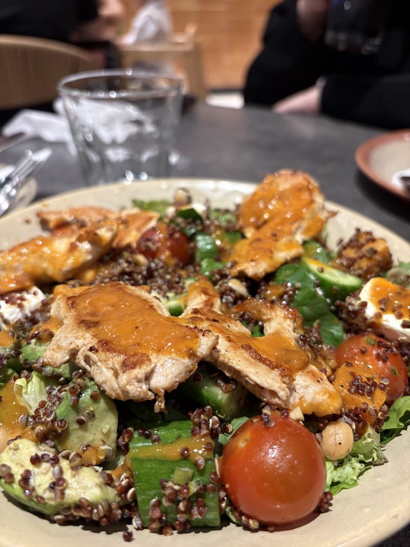 A close-up of a grilled chicken salad with avocado, tomatoes, and quinoa.