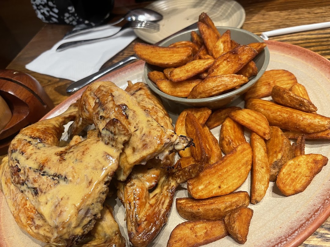 A plate of peri-peri chicken with a creamy sauce and a side of seasoned potato wedges.