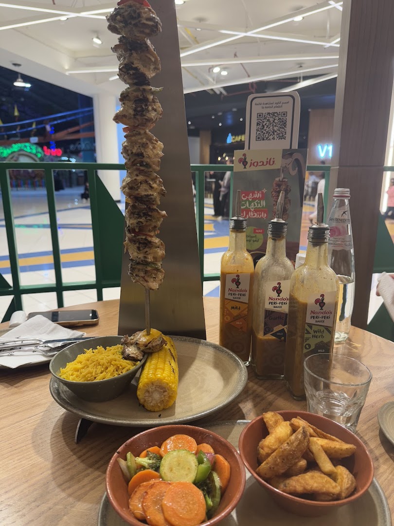A table laden with Nando's peri-peri chicken skewers, rice, corn, fries, and vegetables.