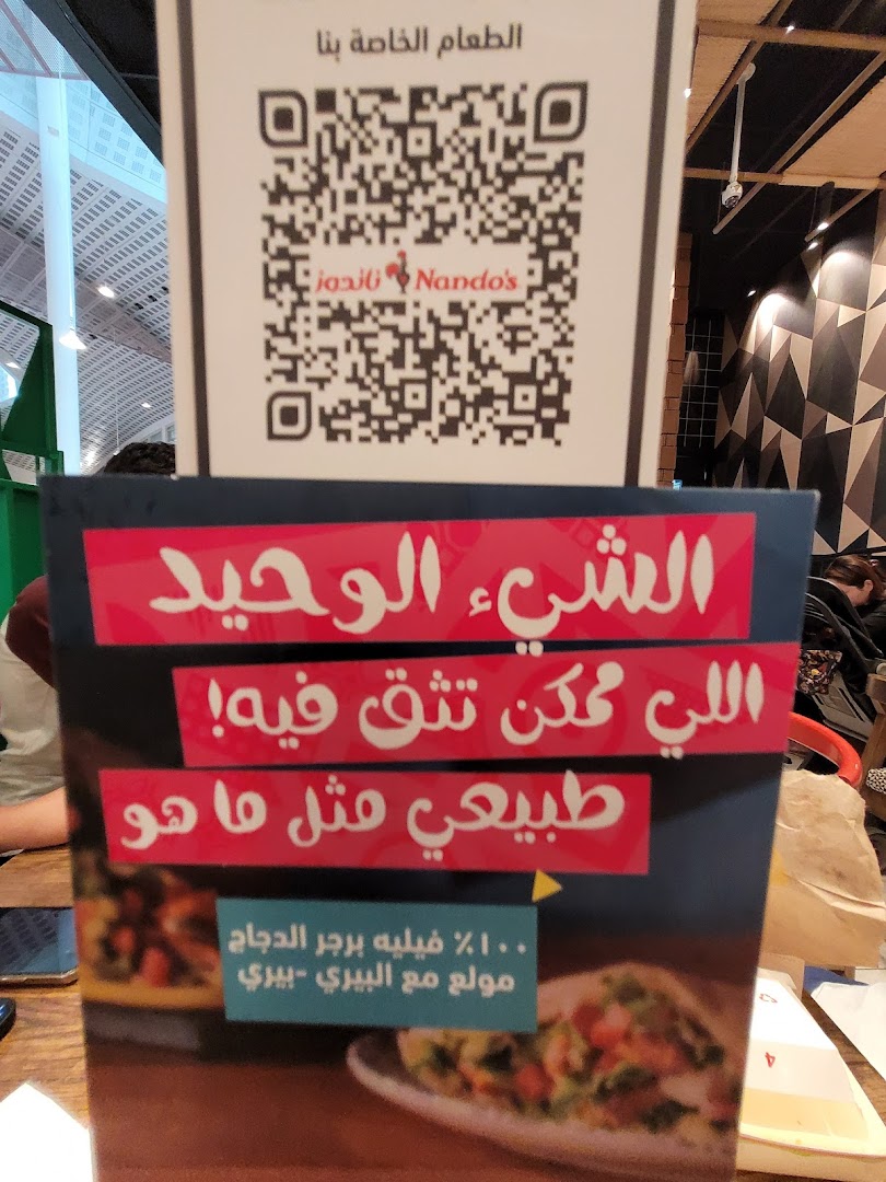 A sign with a QR code and Arabic text promoting Nando's chicken burger.