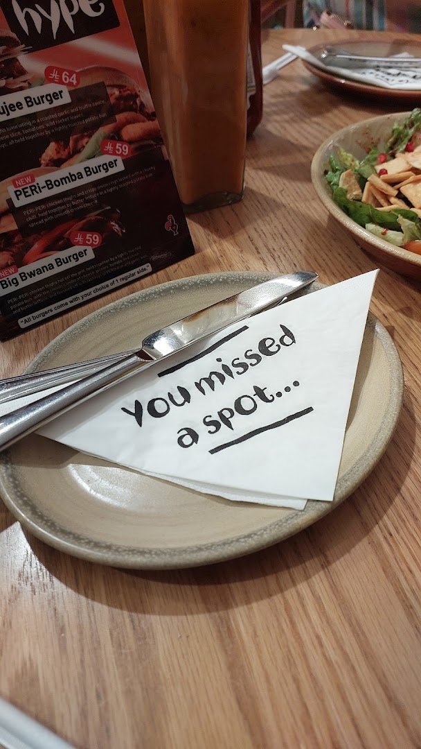 A table setting at Nandos with a menu, cutlery, and a napkin with a message.