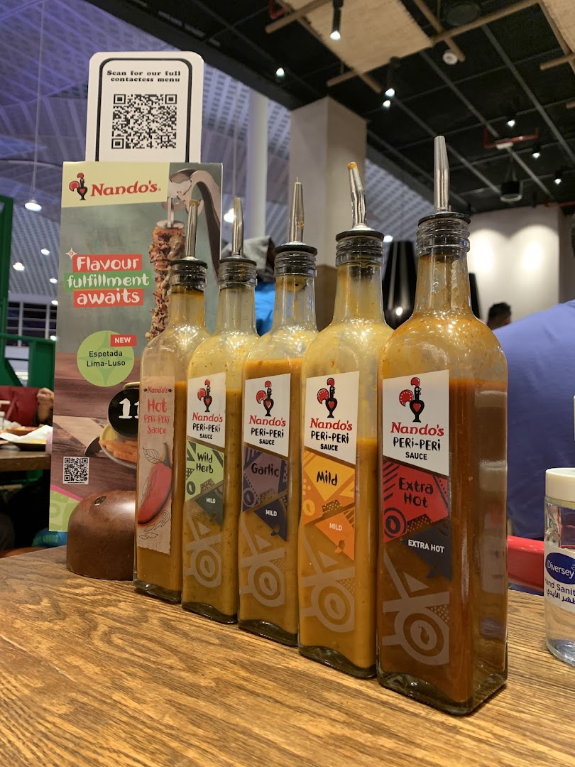 Bottles of Nando's Peri-Peri sauce in various flavors lined up on a wooden table.