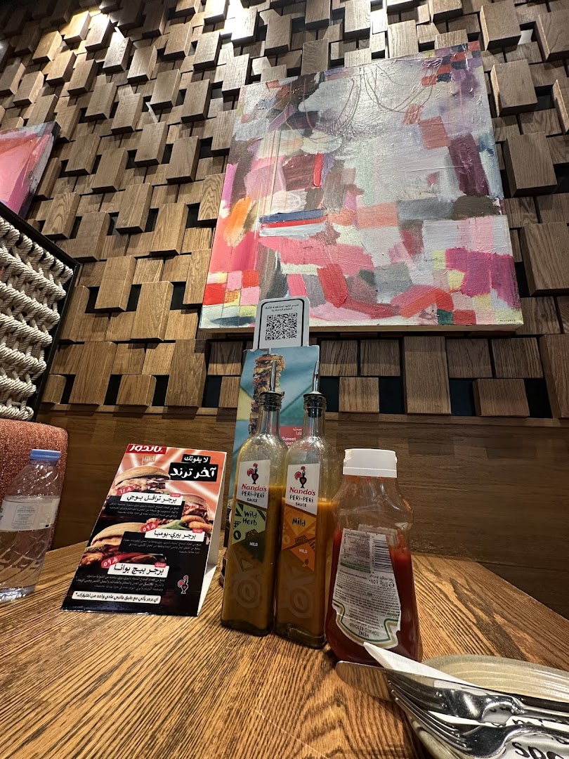A table at Nando's with sauces, a menu, and artwork on the wall.