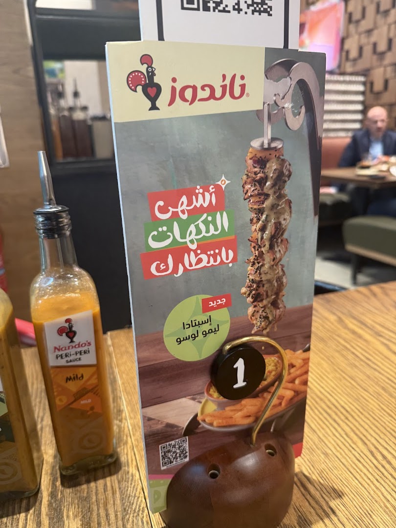 A Nando's menu stand with peri-peri chicken and sauce bottles.