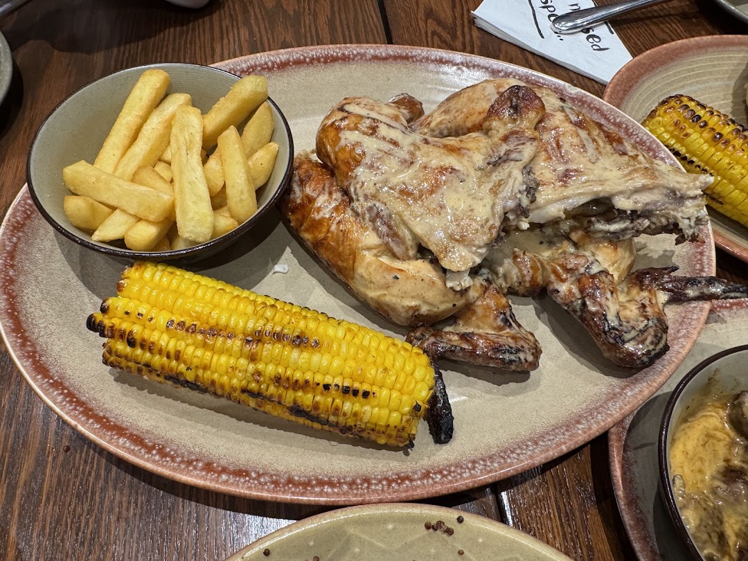 A plate of peri-peri chicken with fries and corn on the cob.
