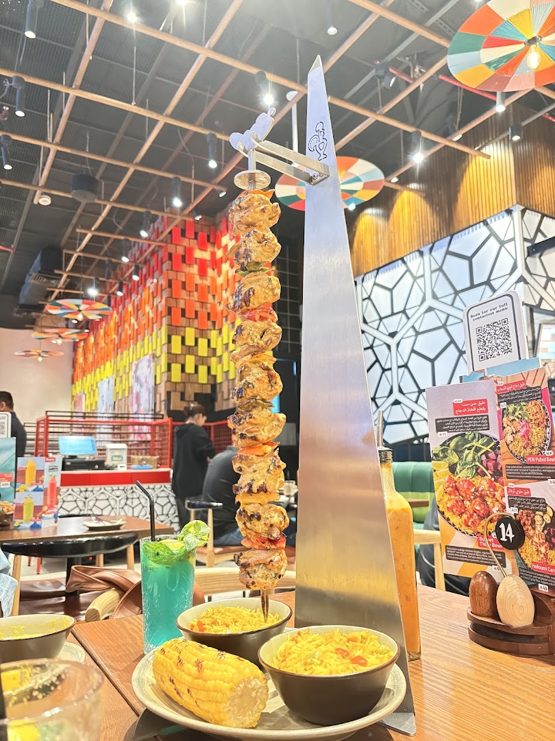 A tall skewer of grilled chicken and shrimp is presented with sides of rice and corn.