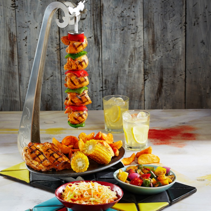 A delicious grilled chicken meal with sides of fries, corn, coleslaw, and grilled vegetables, served with drinks.
