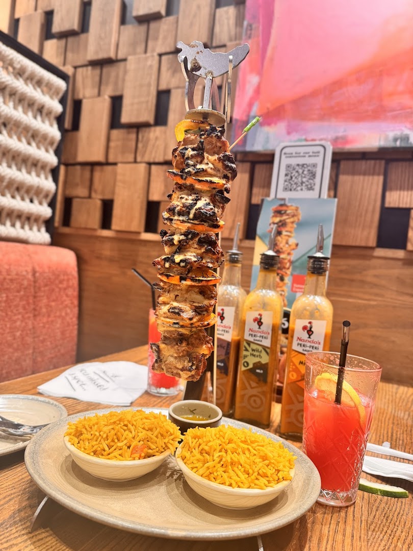 A delicious peri-peri chicken skewer served with rice and a refreshing drink.