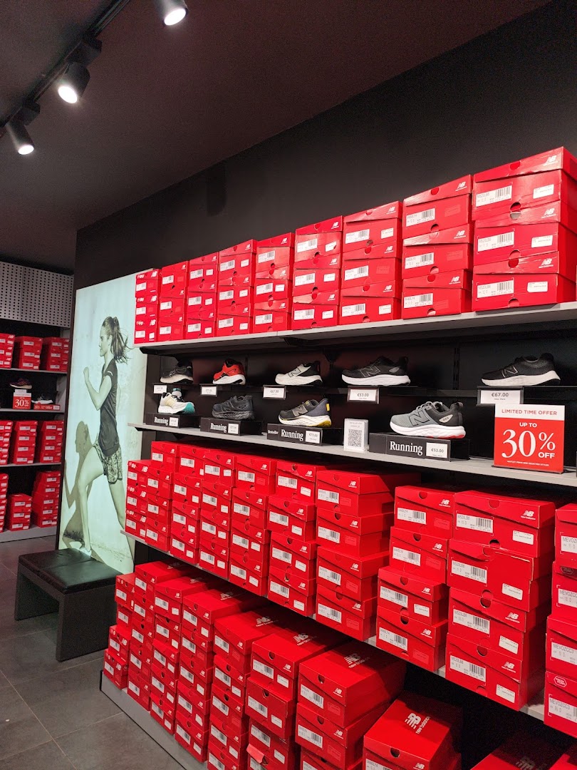 Interior view of a New Balance store showcasing stacks of red shoe boxes and displayed footwear.