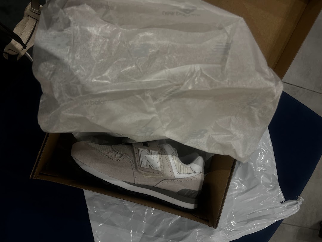 A New Balance sneaker is shown inside its opened box, partially covered by tissue paper.