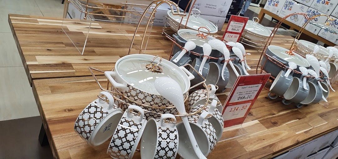 A display of elegant serving dishes and cups with a gold geometric pattern on a wooden table.