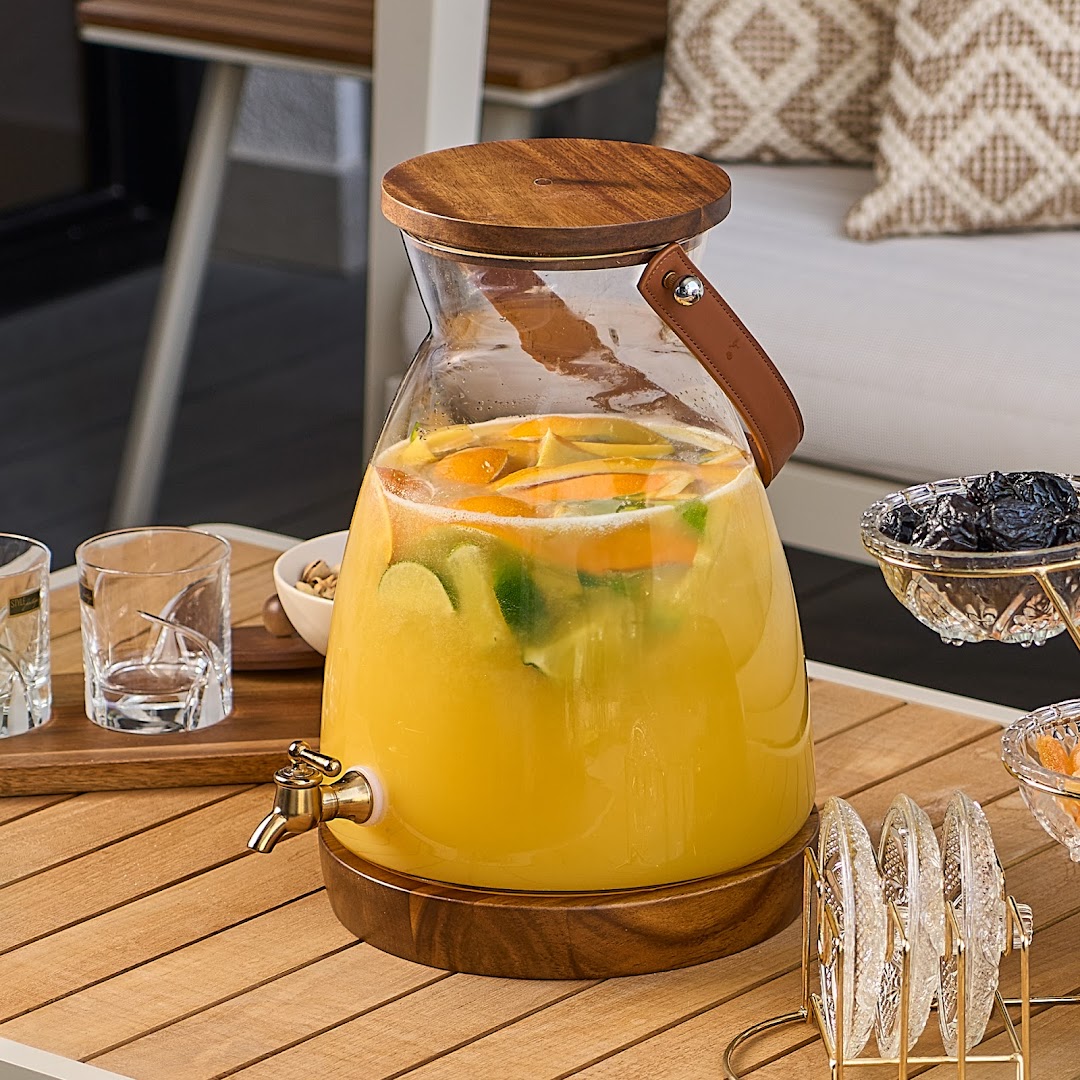 A large glass beverage dispenser filled with citrus-infused orange drink on a wooden table.