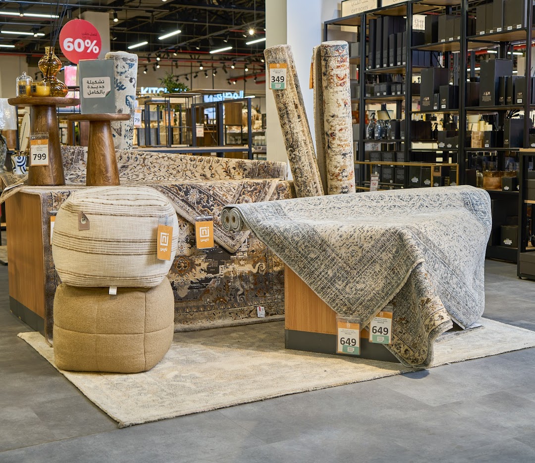 A retail display featuring rolled carpets, poufs, and decorative items with sale signage.