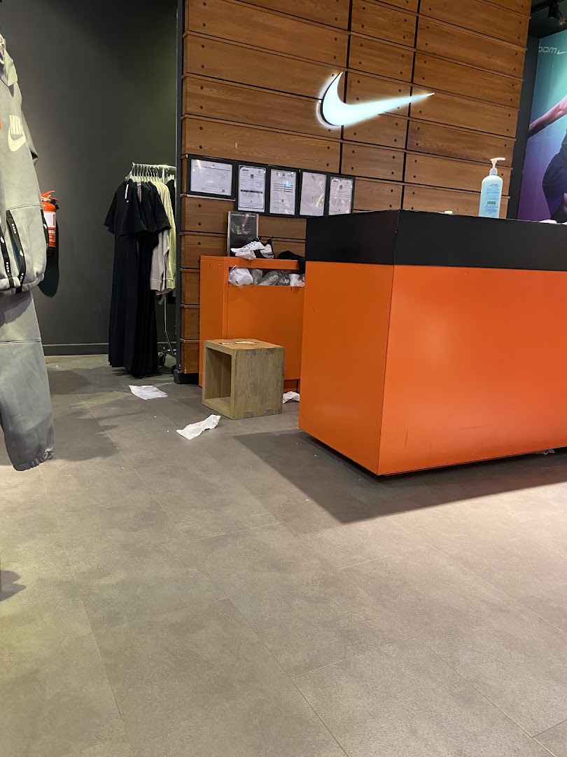 Interior shot of a Nike store with a prominent logo, checkout counter, and clothing racks.