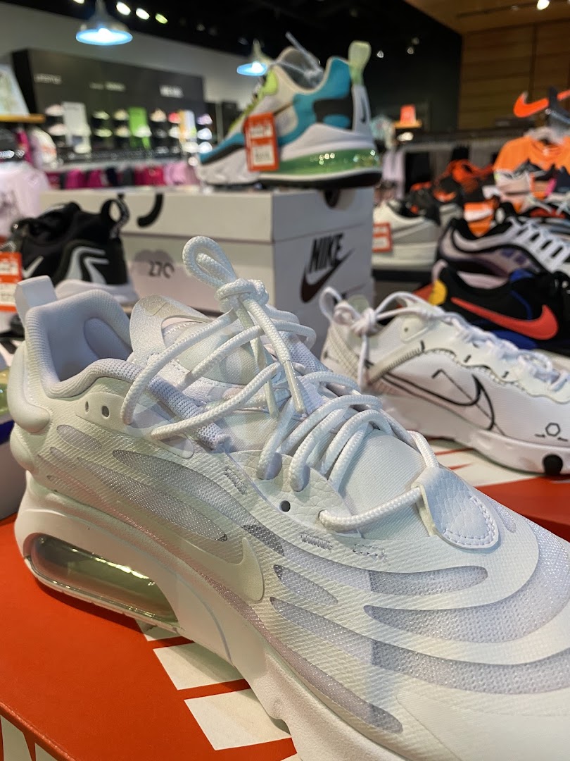 Close-up of white Nike sneakers with other athletic shoes and apparel in the background.