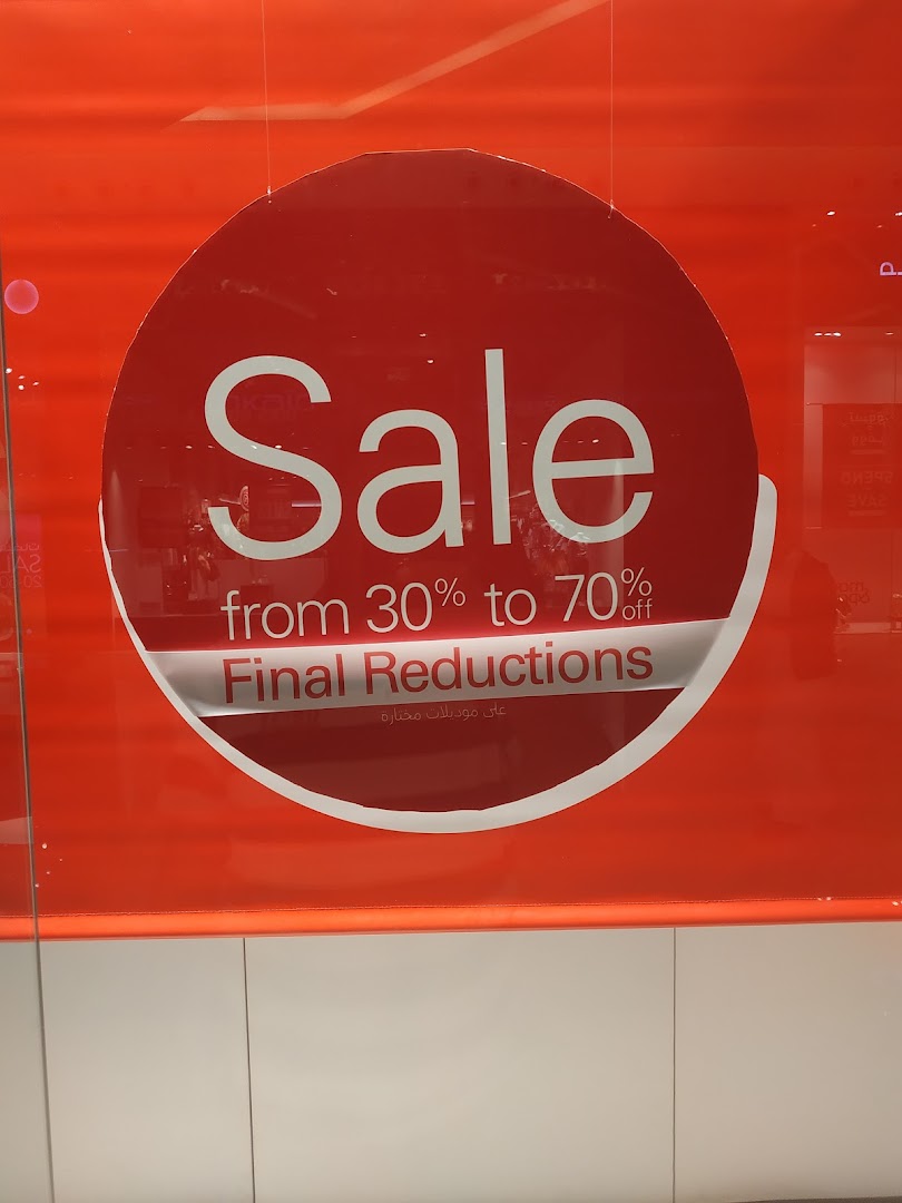 A shop window displays a large red circle with white text announcing a sale.